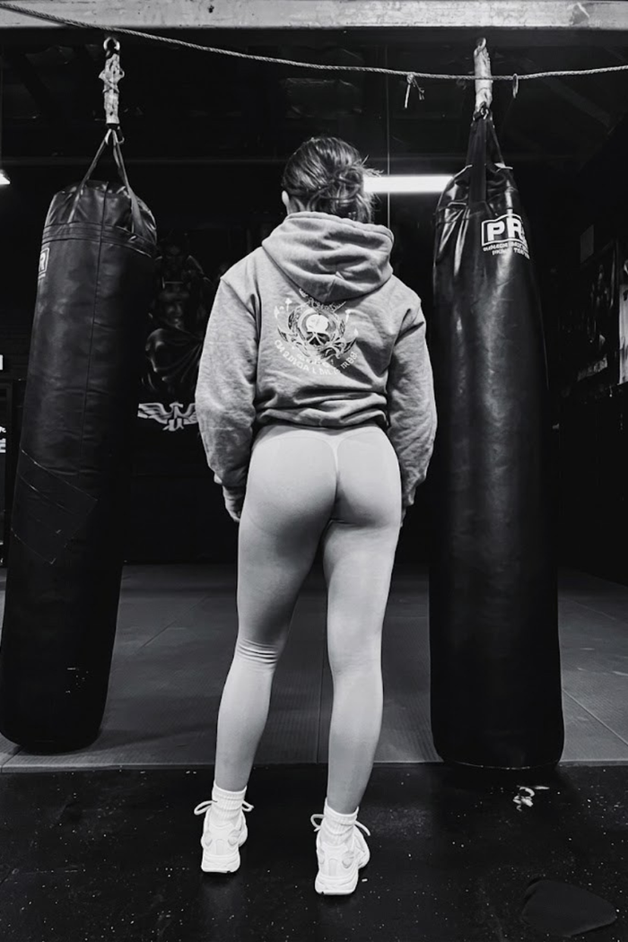 Woman wearing a Grapple Like a Girl hoodie training between heavy bags in a martial arts gym