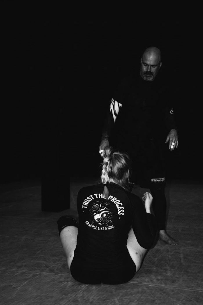 Female grappler training with a coach on the mat wearing a Grapple Like a Girl shirt