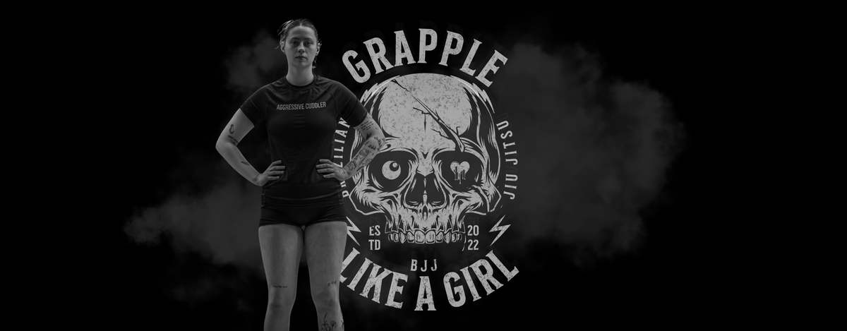 Woman wearing black grappling apparel standing in front of a skull graphic with Grapple Like a Girl branding
